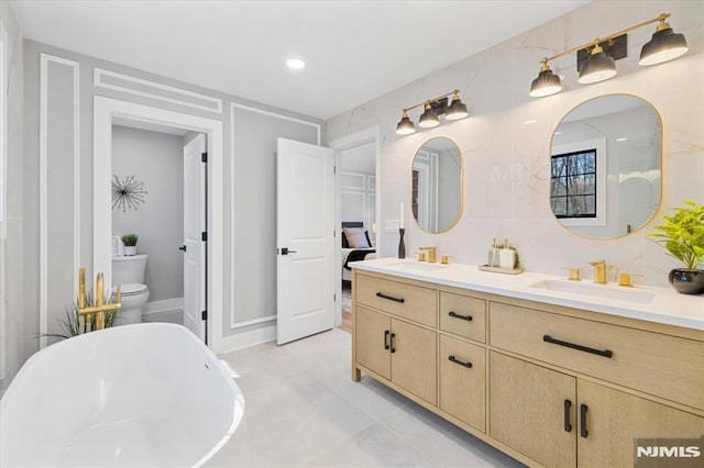 bathroom featuring double vanity, a freestanding bath, toilet, and a sink