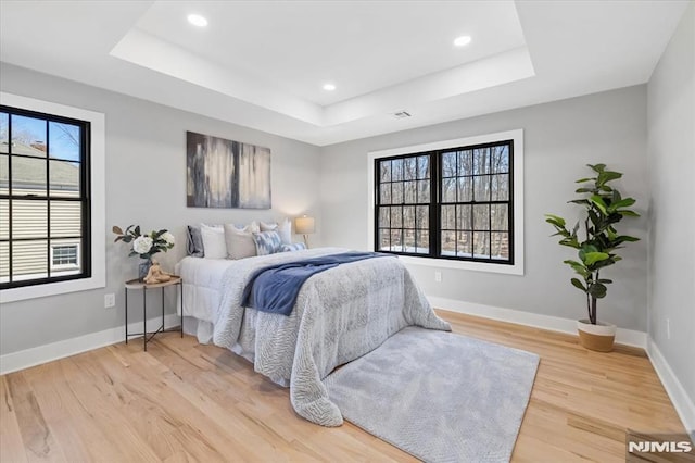 bedroom with light wood finished floors, recessed lighting, a raised ceiling, visible vents, and baseboards