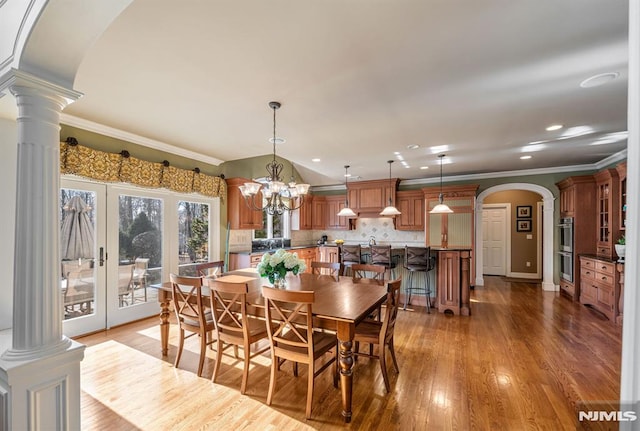 dining space featuring ornate columns, ornamental molding, light hardwood / wood-style floors, and a notable chandelier