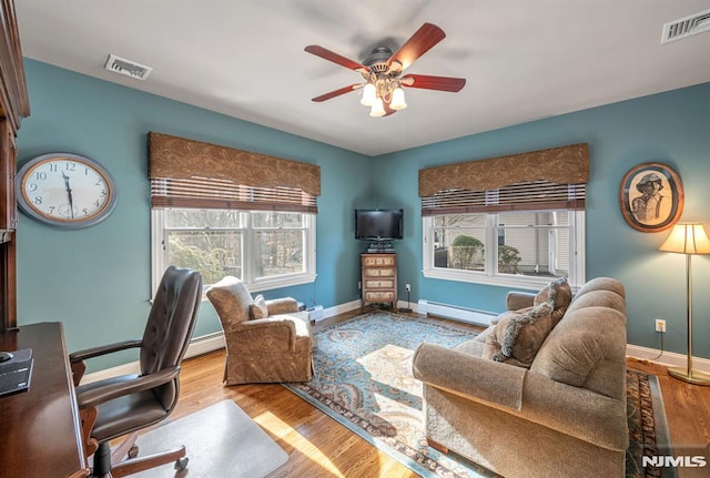 living room featuring a baseboard heating unit, ceiling fan, a wealth of natural light, and light wood-type flooring