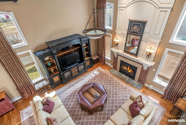 living room featuring a tile fireplace, a baseboard radiator, wood-type flooring, and a healthy amount of sunlight