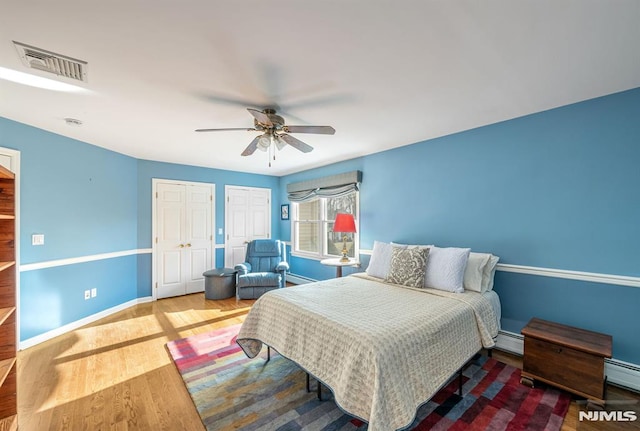 bedroom featuring ceiling fan, baseboard heating, hardwood / wood-style floors, and two closets