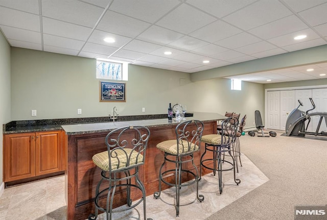 bar featuring light colored carpet, a drop ceiling, dark stone countertops, and sink