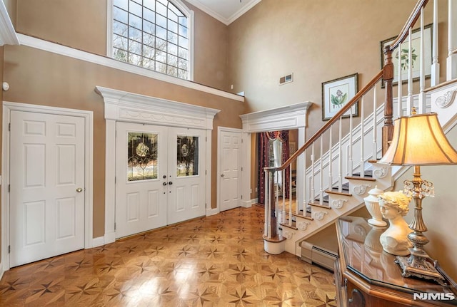 entryway featuring a towering ceiling, french doors, light parquet flooring, ornamental molding, and baseboard heating