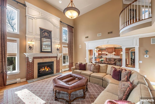 living room with a towering ceiling, a baseboard heating unit, and a healthy amount of sunlight