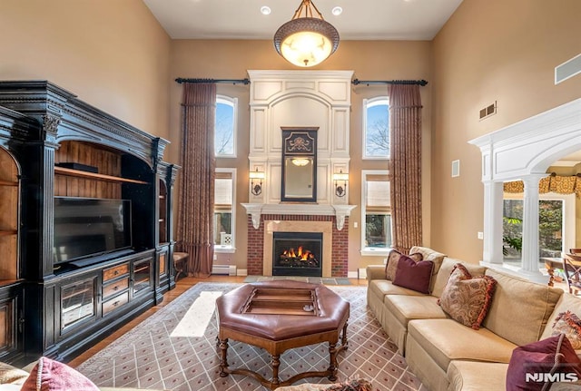 living room with decorative columns, a brick fireplace, a wealth of natural light, a high ceiling, and baseboard heating