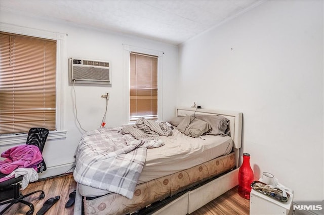 bedroom with hardwood / wood-style floors, a baseboard heating unit, and a wall unit AC