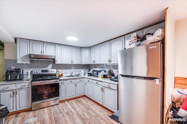 kitchen featuring appliances with stainless steel finishes, gray cabinetry, tasteful backsplash, sink, and light hardwood / wood-style flooring