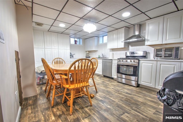 kitchen with appliances with stainless steel finishes, white cabinets, sink, and wall chimney exhaust hood