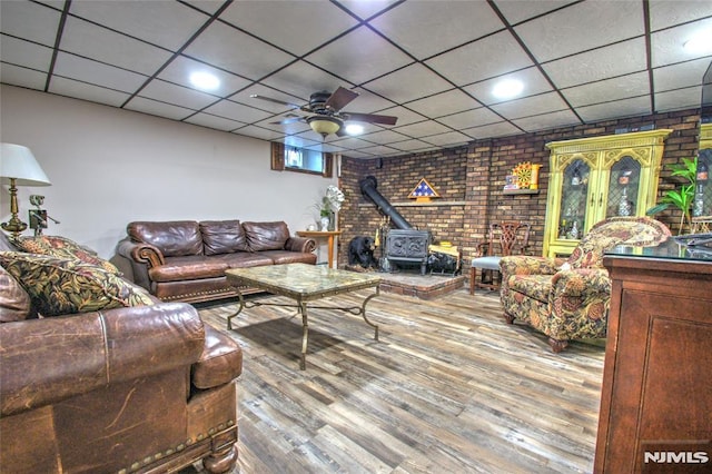 living room featuring brick wall, ceiling fan, a wood stove, and hardwood / wood-style floors