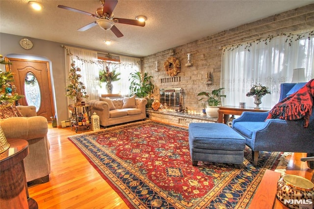 living room featuring a brick fireplace, a textured ceiling, ceiling fan, and hardwood / wood-style floors