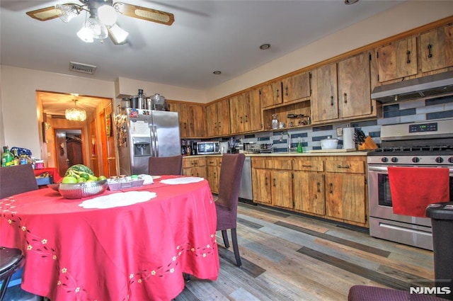 kitchen featuring ceiling fan with notable chandelier, stainless steel appliances, dark wood-type flooring, and backsplash