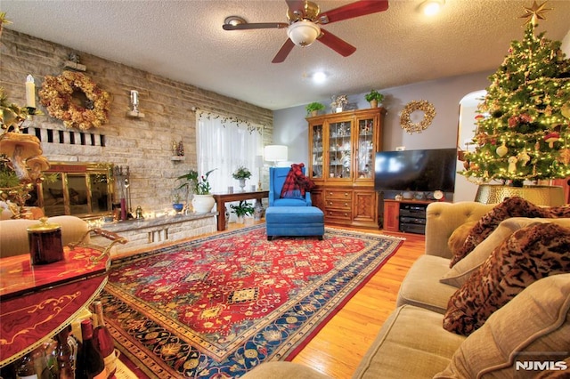 living room featuring a brick fireplace, a textured ceiling, light wood-type flooring, and ceiling fan