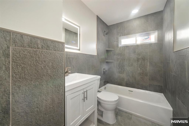 full bathroom with tile walls, toilet, tile patterned floors, vanity, and tiled shower / bath combo