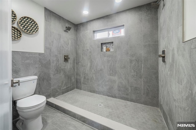 bathroom with tile walls, tile patterned flooring, a tile shower, and toilet