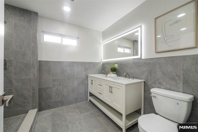 bathroom with tile walls, toilet, tile patterned floors, a shower, and vanity