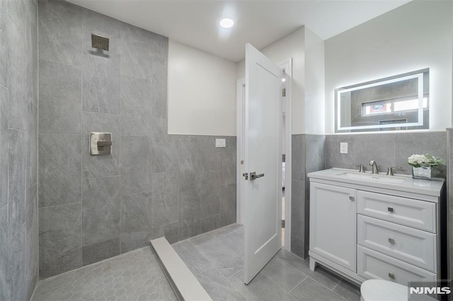 bathroom featuring tile walls, tile patterned flooring, tiled shower, and vanity