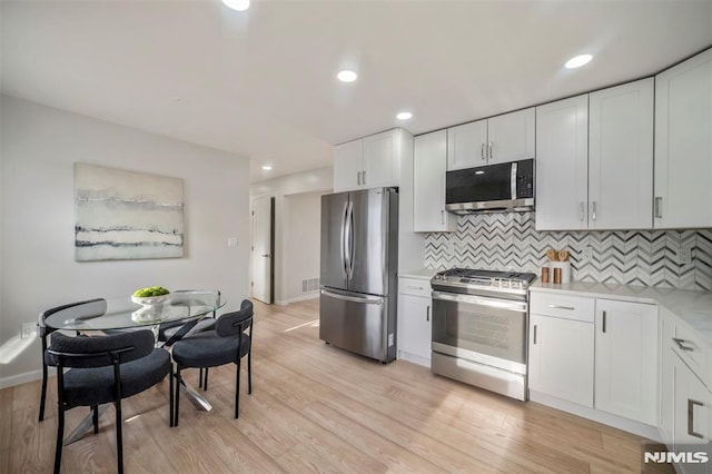 kitchen with appliances with stainless steel finishes, light hardwood / wood-style floors, white cabinets, and backsplash