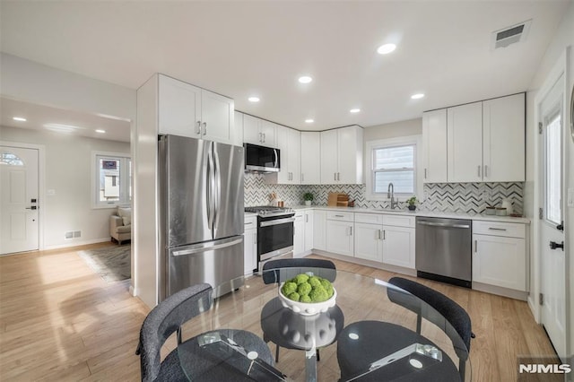 kitchen with sink, appliances with stainless steel finishes, light hardwood / wood-style flooring, and white cabinetry