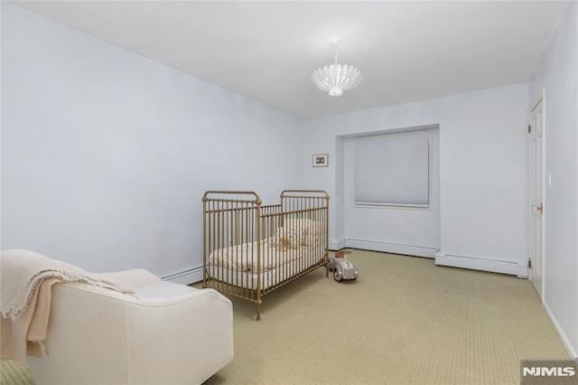 carpeted bedroom with a baseboard heating unit, a crib, and a chandelier