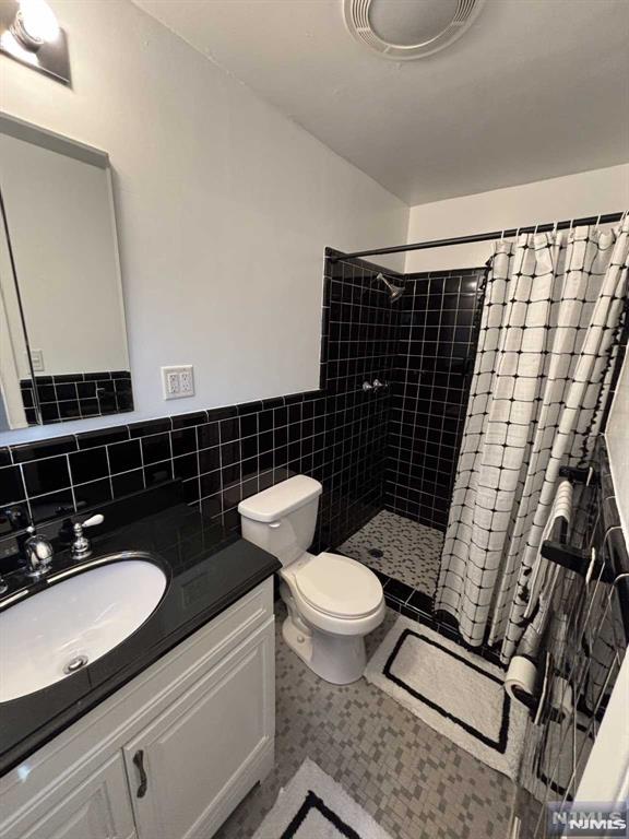 bathroom featuring tile walls, vanity, curtained shower, and toilet