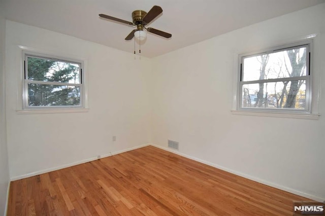 empty room with ceiling fan, a wealth of natural light, and hardwood / wood-style floors