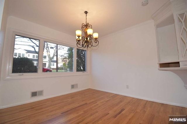 unfurnished dining area featuring ornamental molding, a chandelier, and hardwood / wood-style floors