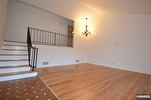 unfurnished living room featuring lofted ceiling, hardwood / wood-style flooring, and a notable chandelier