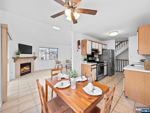 dining room with lofted ceiling, light tile patterned floors, sink, a tile fireplace, and ceiling fan