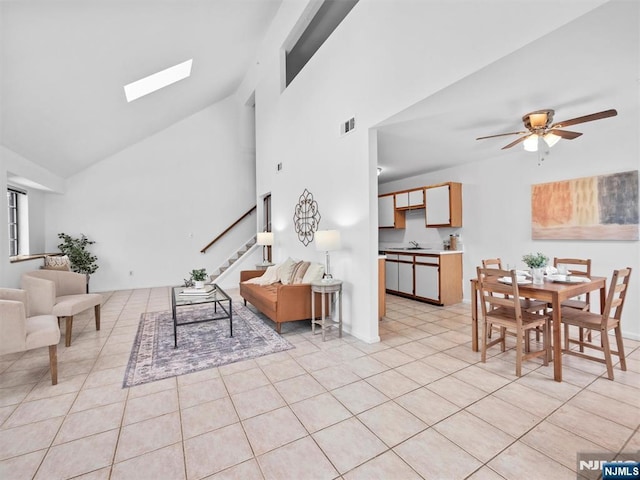 living room featuring high vaulted ceiling, light tile patterned floors, ceiling fan, and a skylight