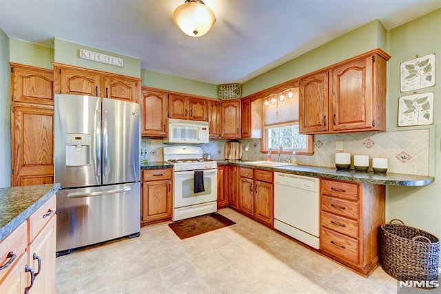 kitchen featuring white appliances, dark stone countertops, backsplash, and sink