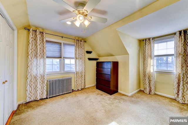 unfurnished bedroom with a closet, light carpet, radiator, ceiling fan, and lofted ceiling