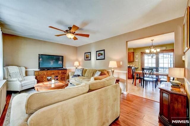 living room with ceiling fan with notable chandelier and light hardwood / wood-style floors