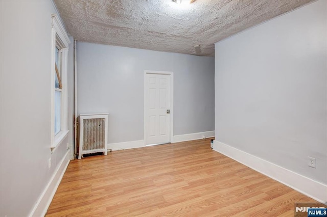 empty room with a textured ceiling and light hardwood / wood-style flooring