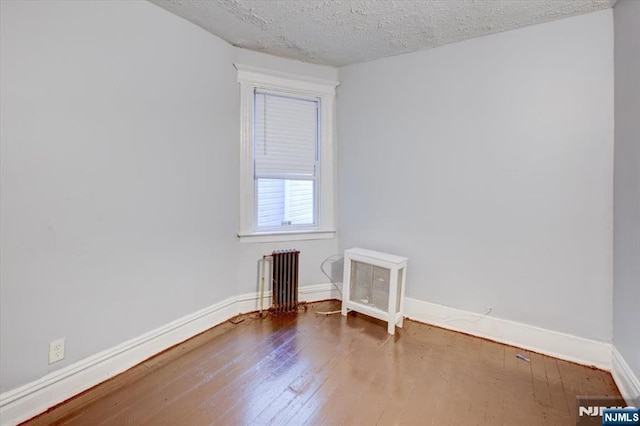 spare room with wood-type flooring, radiator heating unit, and a textured ceiling