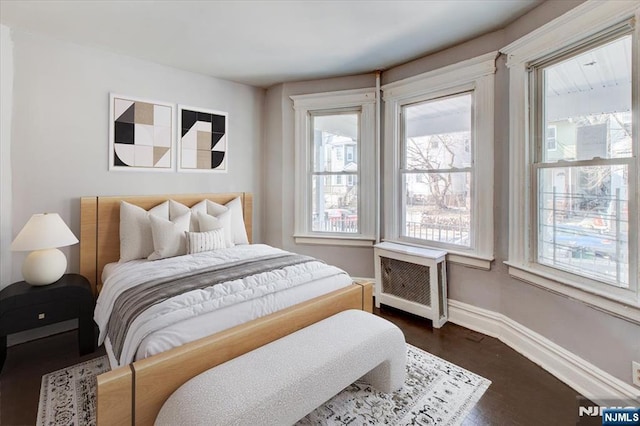 bedroom featuring radiator heating unit, dark wood-type flooring, and multiple windows