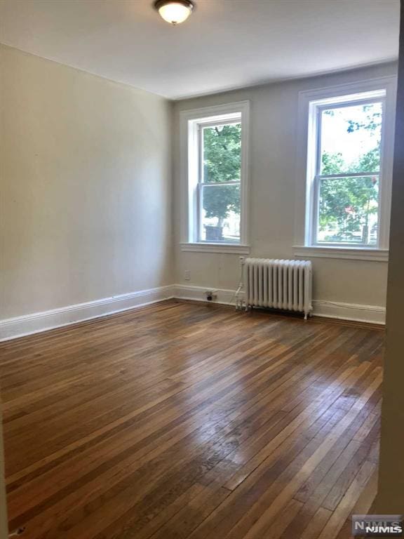 unfurnished room featuring radiator heating unit and dark wood-type flooring