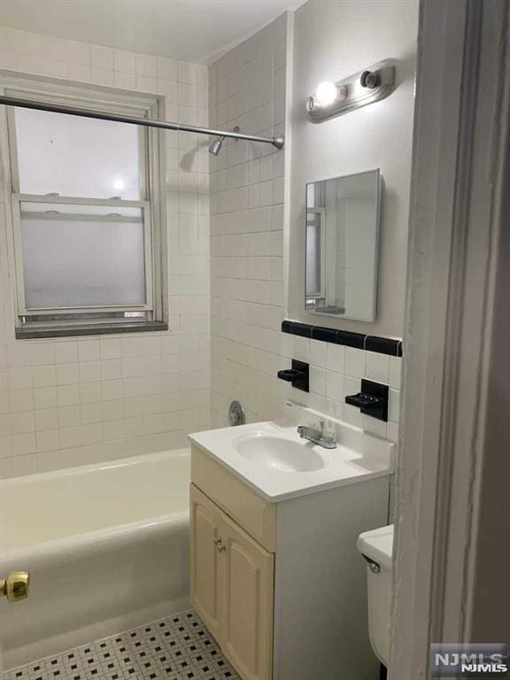 full bathroom featuring toilet, backsplash, tile patterned floors, tiled shower / bath, and vanity