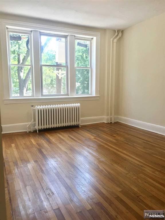 unfurnished room featuring hardwood / wood-style floors, radiator heating unit, and plenty of natural light