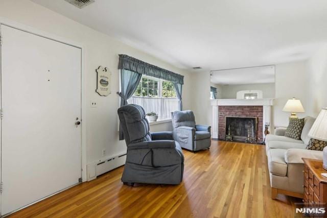 living room featuring baseboard heating, a brick fireplace, and hardwood / wood-style flooring