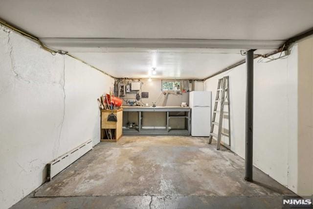 basement with white refrigerator, baseboard heating, and a workshop area