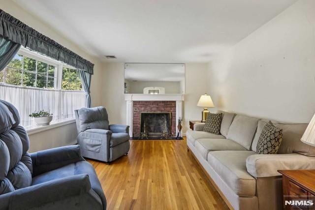 living room featuring a brick fireplace, light wood-type flooring, and a wealth of natural light