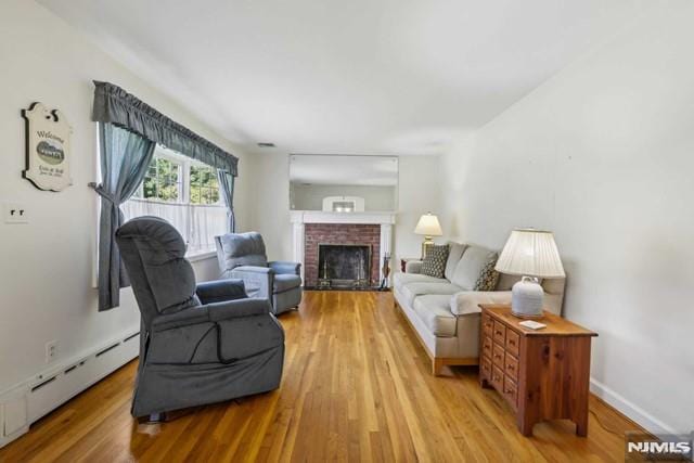 living room featuring a baseboard radiator, a brick fireplace, and light hardwood / wood-style floors