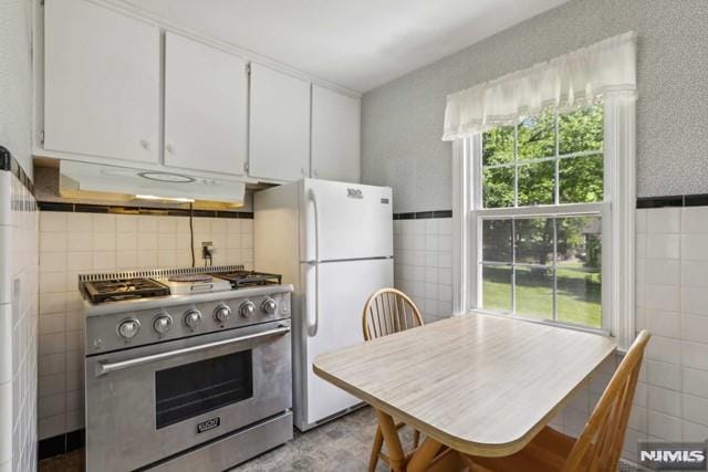 kitchen with high end stainless steel range oven, tile walls, white cabinetry, and white fridge