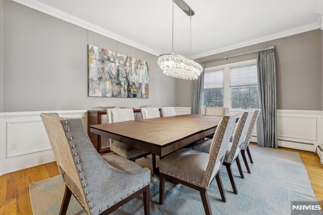 dining room with ornamental molding, wood finished floors, an inviting chandelier, wainscoting, and a decorative wall