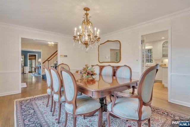 dining area with light wood-style flooring, an inviting chandelier, ornamental molding, and stairs