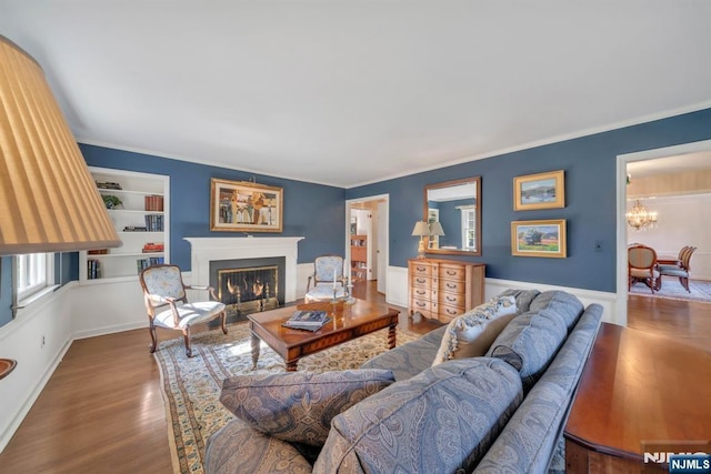 living area with a glass covered fireplace, ornamental molding, wood finished floors, and a chandelier