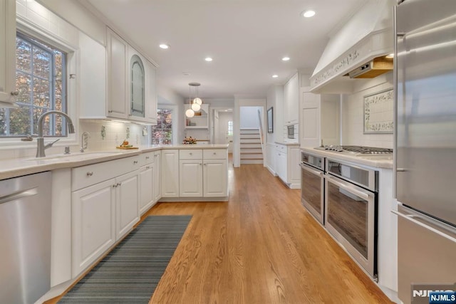 kitchen featuring white cabinetry, appliances with stainless steel finishes, wall chimney exhaust hood, and light countertops