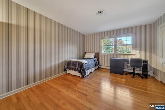 bedroom featuring visible vents, wallpapered walls, light wood finished floors, a baseboard radiator, and baseboards