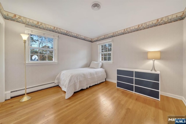 bedroom with a baseboard heating unit, wood finished floors, visible vents, and baseboards